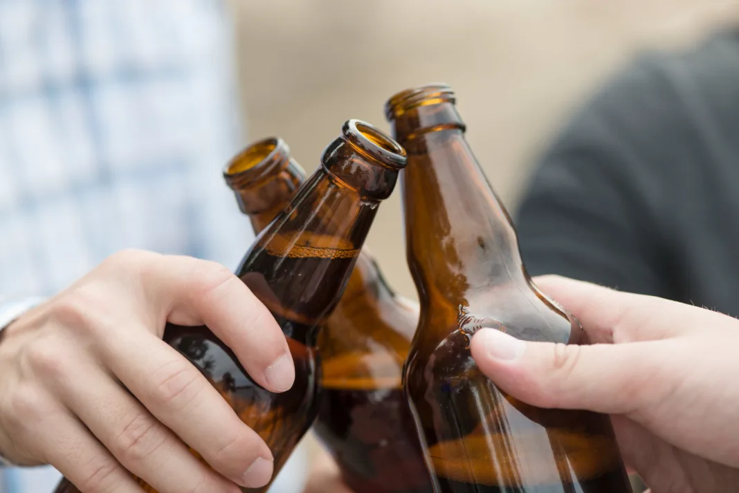 Ludzie stukający się butelkami piwa – symboliczna scena spożywania alkoholu w grupie