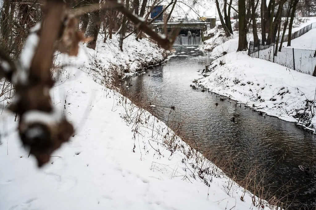 budowa ścieżki nad Zalewem Zadębie . Zimowy widok na rzekę wypływającą z Zalewu Zadębie. W tle widoczny jaz (tama) kończący zbiornik, obok którego powstanie ścieżka rowerowa.