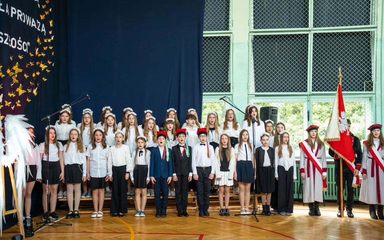 Występ artystyczny uczniów podczas oficjalnej akademii z okazji 110-lecia SP 2 w Skierniewicach, na scenie baner jubileuszowy.