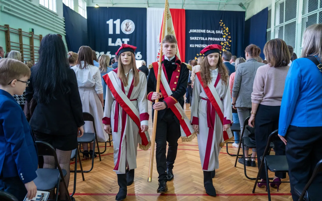 Występ artystyczny uczniów podczas oficjalnej akademii z okazji 110-lecia SP 2 w Skierniewicach, na scenie baner jubileuszowy.