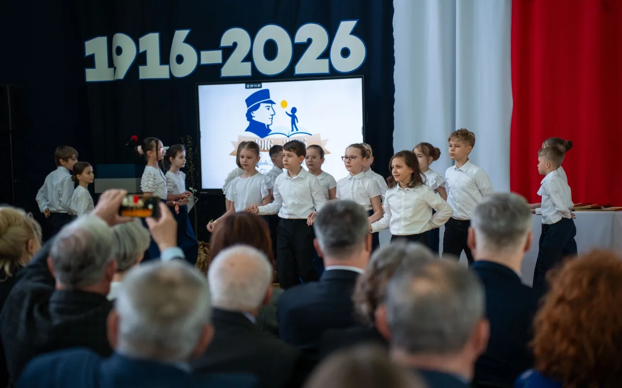 Występ artystyczny uczniów podczas oficjalnej akademii z okazji 110-lecia SP 2 w Skierniewicach, na scenie baner jubileuszowy.