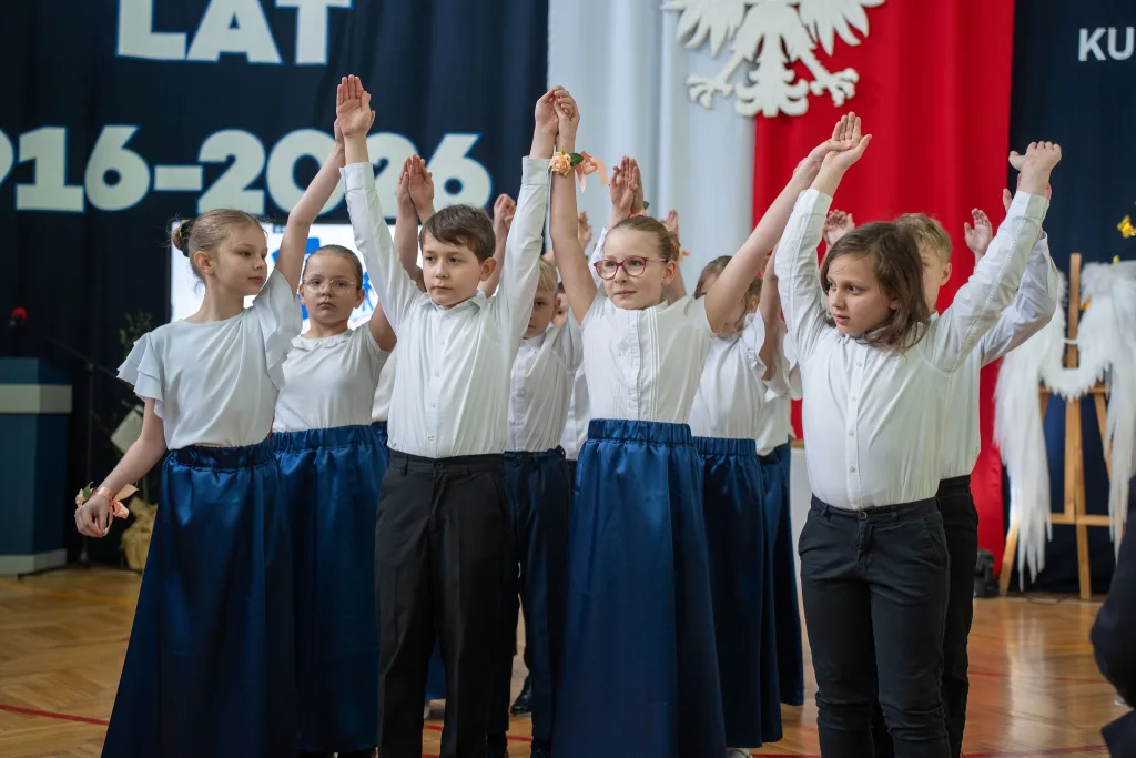Występ artystyczny uczniów podczas oficjalnej akademii z okazji 110-lecia SP 2 w Skierniewicach, na scenie baner jubileuszowy.