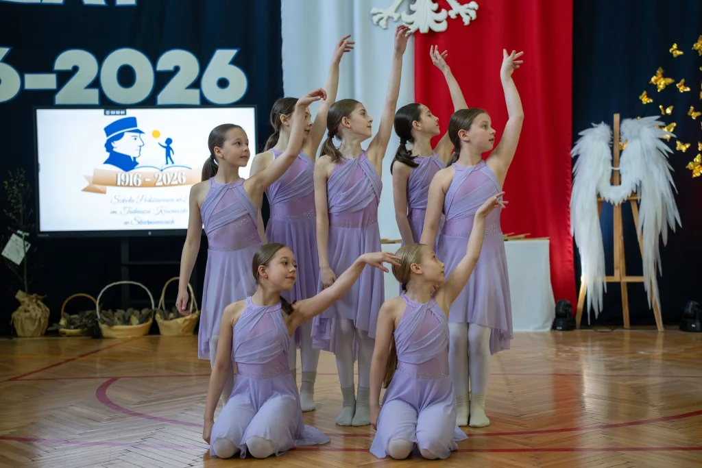Występ artystyczny uczniów podczas oficjalnej akademii z okazji 110-lecia SP 2 w Skierniewicach, na scenie baner jubileuszowy.