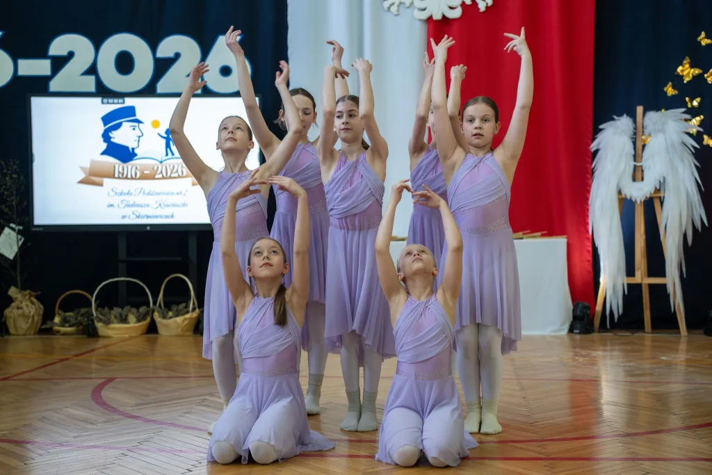 Występ artystyczny uczniów podczas oficjalnej akademii z okazji 110-lecia SP 2 w Skierniewicach, na scenie baner jubileuszowy.
