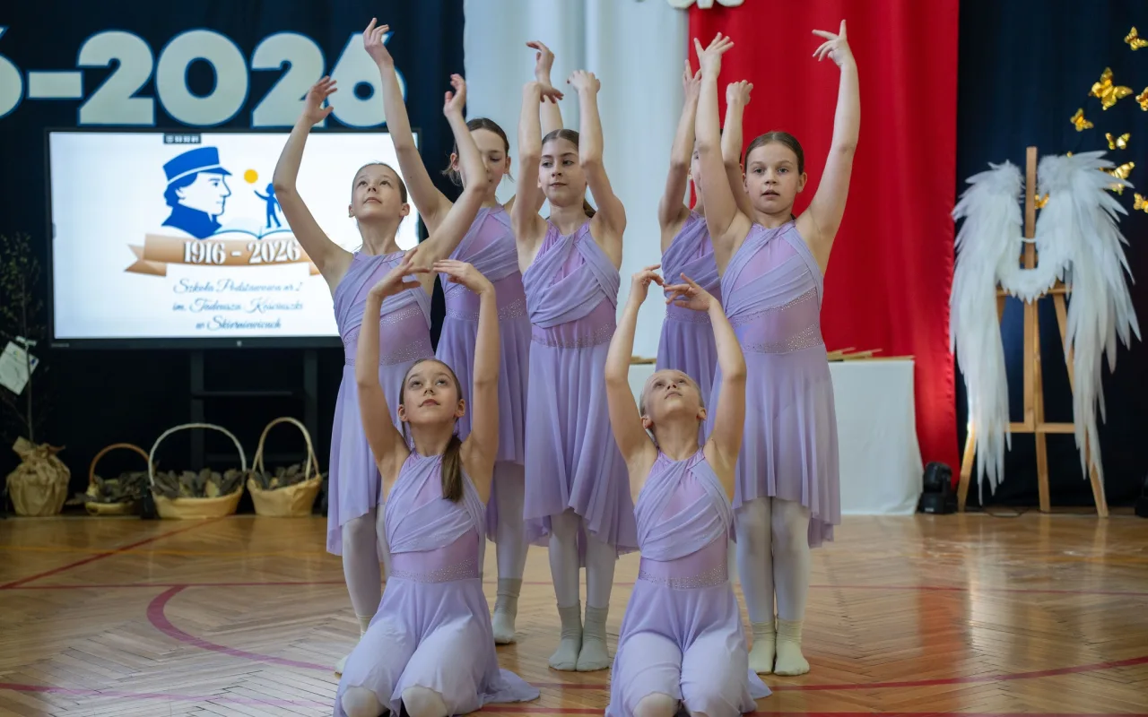 Występ artystyczny uczniów podczas oficjalnej akademii z okazji 110-lecia SP 2 w Skierniewicach, na scenie baner jubileuszowy.