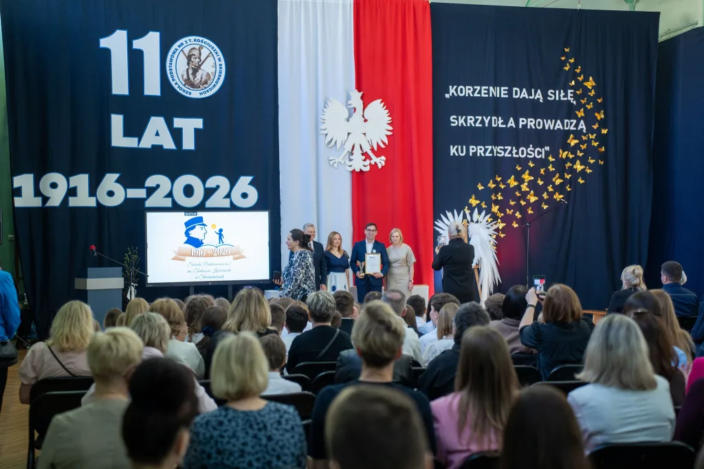 Występ artystyczny uczniów podczas oficjalnej akademii z okazji 110-lecia SP 2 w Skierniewicach, na scenie baner jubileuszowy.