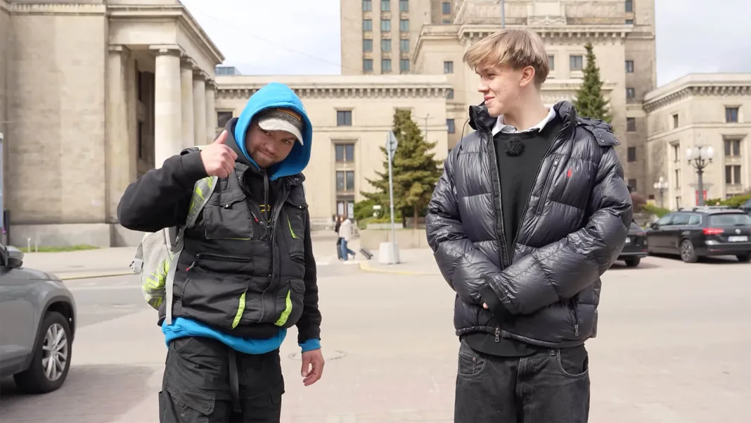 Uśmiechnięty youtuber i bezdomny Sebastian pokazujący kciuk w górę podczas nagrywania filmu na ulicach Warszawy.