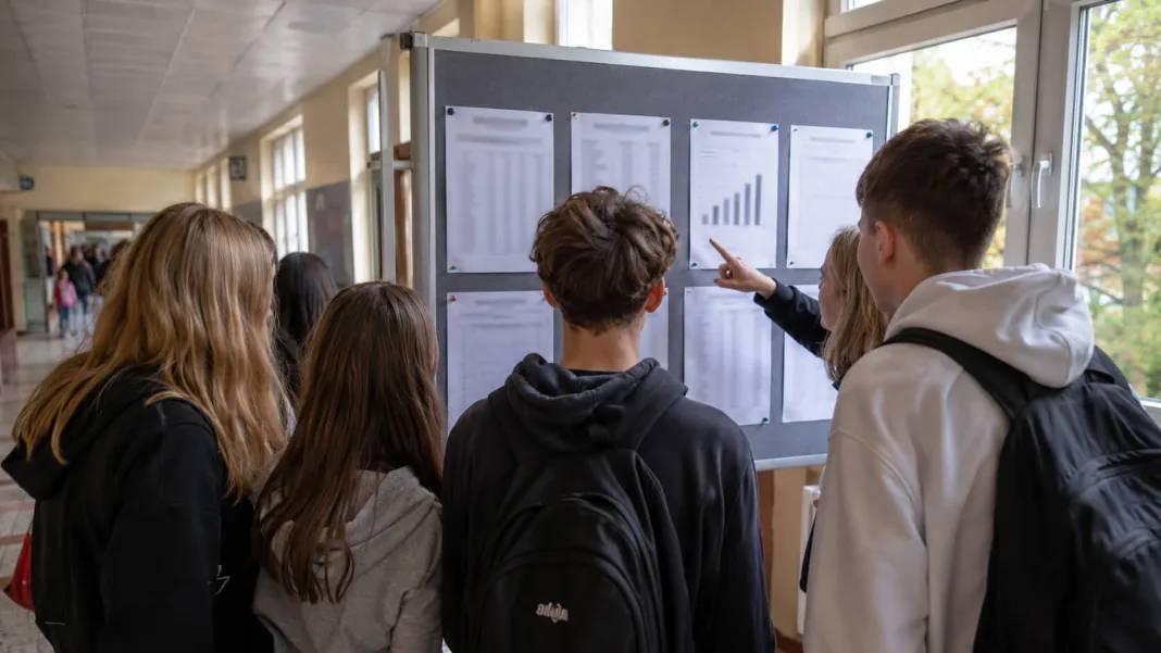 Uczniowie szkoły podstawowej oglądają wyniki egzaminu ósmoklasisty na tablicy informacyjnej.